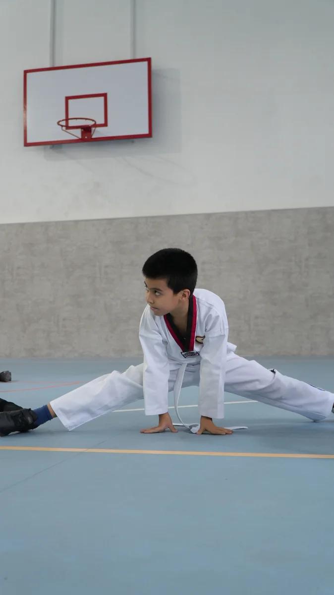 Taekvondo mashgʻulotida shpagat qilayotgan bola